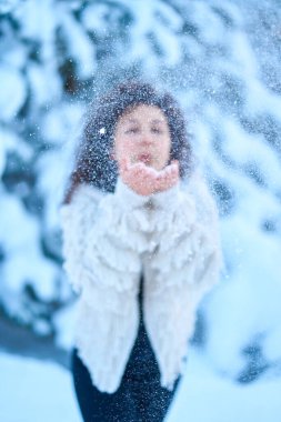 Karla kaplı bir kış ormanında mutlu bir kadın karla oynuyor..