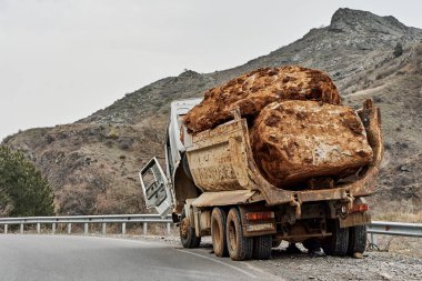 Sırtında büyük bir taş taşıyan eski bir kamyon bir dağ yolunda bozuldu..