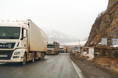 Karla kaplı dağlarda bir kamyon kuyruğu geçidin açılmasını bekliyor. Malların zor hava koşullarında nakliyesi. Bu yüzden paketin gecikti. Gudauri, Gürcistan - 04.07.2021