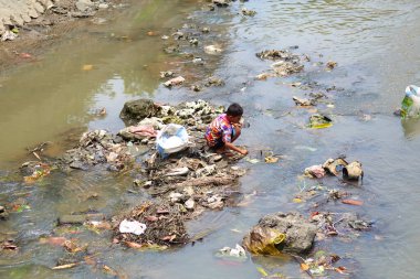 Bir adam değerli bir şey bulmak için nehirde yüzen çöpleri karıştırıyor. Bali, Endonezya - 03.01.2018