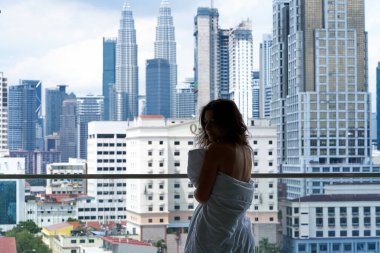 Büyük şehirde bir sabah. Şehir merkezindeki balkonundan manzaranın tadını çıkaran battaniyeli bir kız..