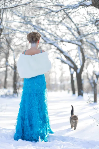 fairytale cosplay on snow queen. Woman in the dress posing in the snowy forest with a cat.