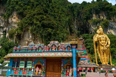A huge golden statue of Lord Murugan at the entrance with multicolored steps to the Batu Caves. Kuala Lumpur, Malaysia - 11.09.2022