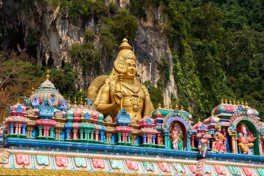 A huge golden statue of Lord Murugan at the entrance with multicolored steps to the Batu Caves. Kuala Lumpur, Malaysia - 11.09.2022