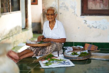 Balili bir kadın ön bahçesinde otururken koka yapraklarını öğütüyor. Bali, Endonezya - 03.23.2018