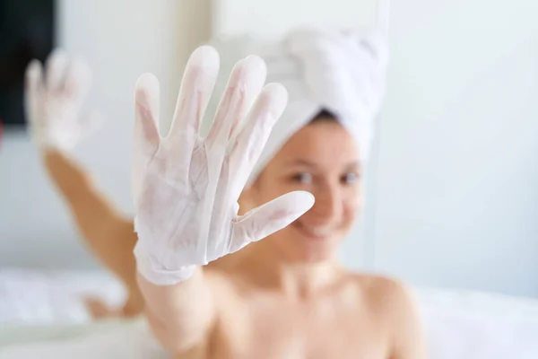 シャワーの後 タオルに包まれた女の子は彼女の手の皮膚を潤すために化粧品の手袋を使用しています 家庭でのボディケアのための化粧品の傾向 — ストック写真
