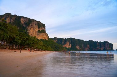 Deniz kıyısında gün batımı. Sahildeki dalgalar ve yürüyen insanlarla dolu. Tayland, Krabi - 10.12.2022