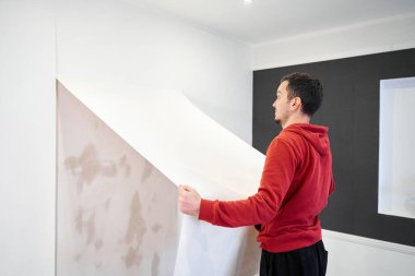 Repair the house with their own hands. The guy is ripping the old wallpaper off the wall.