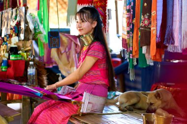 Uzun boyunlu bir kabileden bir kadının portresi, boyunlarındaki metal halkalarla tanınıyor, renkli bir battaniye örüyor. Kültürel çeşitliliği ve geleneği kutluyor. Chiang Rai, Tayland - 09.02.2022