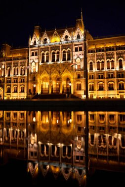Budapeşte 'deki parlamento binasının aydınlatılmış cephesinin muhteşem bir gece fotoğrafı suya yansıdı. Budapeşte, Macaristan - 08.24.2022