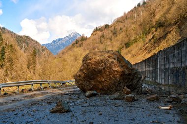 A huge rock fell from the mountains onto the road, destroying the asphalt and blocking half of the roadway.
