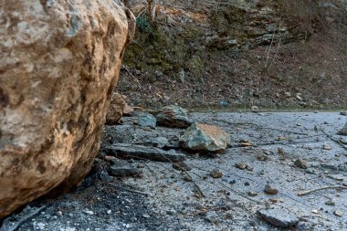 A huge rock fell from the mountains onto the road, destroying the asphalt and blocking half of the roadway.