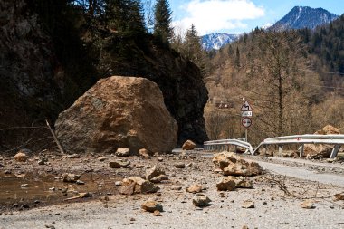 A huge rock fell from the mountains onto the road, destroying the asphalt and blocking half of the roadway. clipart