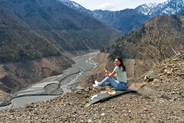 A girl on a picnic with an incredible natural view of the mountains and a dehydrated mountain river. Gorgeous scenery.