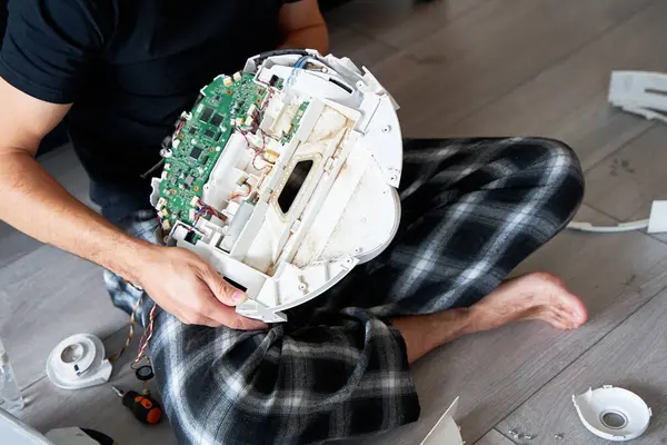 Repair of a robot vacuum cleaner that is clogged with dirt and wool. A male repairman holds a disassembled robot vacuum cleaner. the concept of repairing home electronics