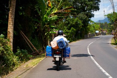 Bir motosikletli Asya 'da manzaralı asfalt bir yolda gidiyor. Bali, Endonezya - 12.08.2022