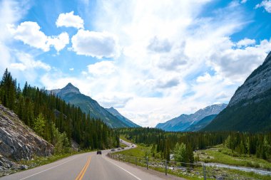 Alberta 'daki Banff Ulusal Parkı' ndaki Rocky Dağları 'ndan güzel bir manzara. Yazın güneşli bir günde, kozalaklı bir ormanı geçtikten sonra dağlardaki bir yolun manzarası.