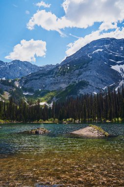 İnanılmaz güzel şeffaf zümrüt göl. Kara Prens Sirk Yolu 'ndaki kayalık dağın yansıması. Güneşli yaz gününde Alberta, Kananaskis 'te kar yağan görkemli Kanada dağları.