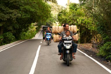 İnsanlar çok yüklü bir motosiklet kullanıyor. Asyalılar küçük işletmeleri için mal taşıyorlar. Bali, Endonezya - 12.09.2022