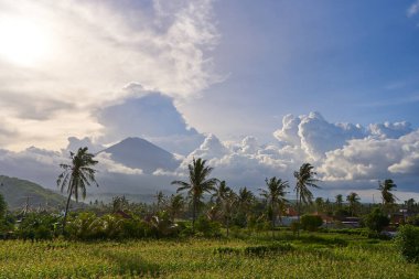 Dağın arka planında palmiye ağaçları ve mısır tarlaları var. Gün batımından önce Agung volkanı bulutlarla kaplıydı.