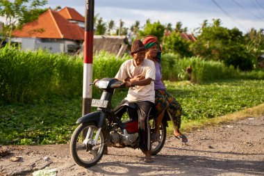 Bali 'de bir köyde motosiklet süren pitoresk yaşlı bir çift. Bali, Endonezya - 12.10.2022