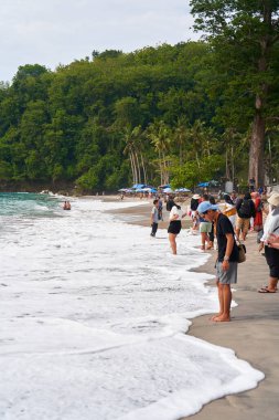 Bir grup turist tropikal bir plajda yürür ve fotoğraf çeker. Bali, Endonezya - 12.30.2022