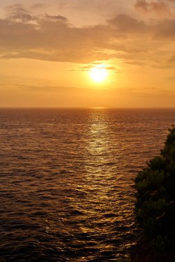 Gün batımında dağ ve okyanus manzarası. Denizin üzerinde güneşli bir yol