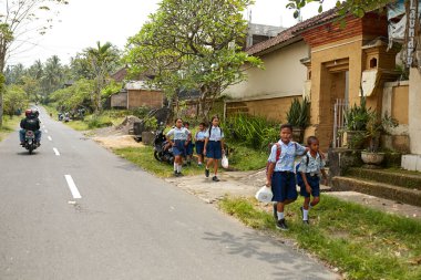 Bir grup üniformalı çocuk Asya 'daki bir Endonezya köyünde bir yol boyunca okuldan yürüyorlar. Bali, Endonezya - 03.22.2018