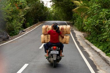 İnsanlar çok yüklü bir motosiklet kullanıyor. Asyalılar küçük işletmeleri için mal taşıyorlar. Bali, Endonezya - 12.09.2022