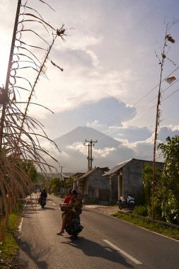 Köyde tatil için dekore edilmiş yol volkanının manzarası. Yol boyunca bambu süslemeleri. Gün batımından önce Agung Dağı 'nın bulutlarla kaplı bir manzarası. Bali, Endonezya - 12.10.2022