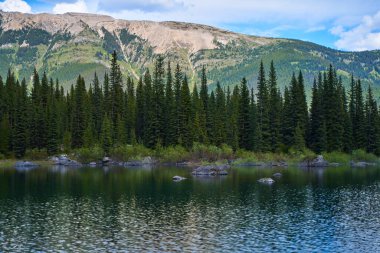 İnanılmaz güzel şeffaf zümrüt göl. Kara Prens Sirk Yolu 'ndaki kayalık dağın yansıması. Güneşli yaz gününde Alberta, Kananaskis 'te kar yağan görkemli Kanada dağları.
