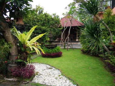 A traditional wooden gazebo sits in a lush tropical garden. clipart