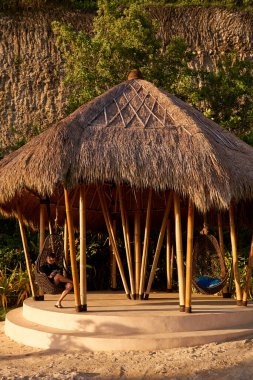 Bir adam saman pergola 'da sallanan bir yumurtada oturur ve günbatımının tadını çıkarır.