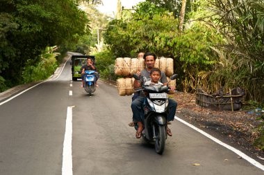 İnsanlar çok yüklü bir motosiklet kullanıyor. Asyalılar küçük işletmeleri için mal taşıyorlar. Bali, Endonezya - 12.09.2022