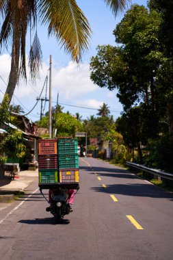 İnsanlar çok yüklü bir motosiklet kullanıyor. Asyalılar küçük işletmeleri için mal taşıyorlar. Bali, Endonezya - 12.10.2022