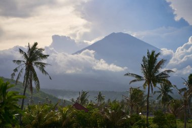 Dağın arka planında palmiye ağaçları ve mısır tarlaları var. Gün batımından önce Agung volkanı bulutlarla kaplıydı.