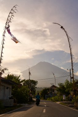 Köyde tatil için dekore edilmiş yol volkanının manzarası. Yol boyunca bambu süslemeleri. Gün batımından önce Agung Dağı 'nın bulutlarla kaplı bir manzarası. Bali, Endonezya - 12.10.2022