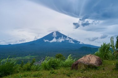 Büyük taşlı bir bakış açısı ve Bali adasındaki yağmurlu bir günde Agung 'un bulutlarla kaplı kutsal volkanı. Dağın manzarası