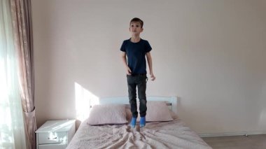 Rahat bir yatakta zıplayan gülümseyen çocuk.