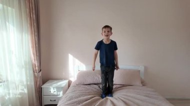 Çocuk yatakta zıplıyor, eğleniyor.
