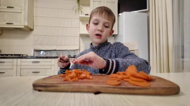 Çocuk mutfakta yemek hazırlıyor, salata için haşlanmış havuç kesiyor.