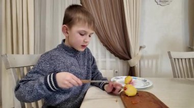 Çocuk mutfakta yemek hazırlıyor, salata için haşlanmış patates kesiyor.