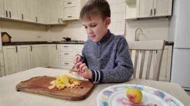 Çocuk mutfakta yemek hazırlıyor, salata için haşlanmış patates kesiyor.