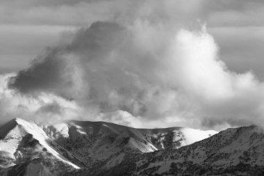 Ormanlı karlı dağlara ve kış akşamında güneşli bulutlu gökyüzüne bakın. Kafkas Dağları. Gürcistan, Gudauri bölgesi. Siyah ve beyaz tonlu manzara.