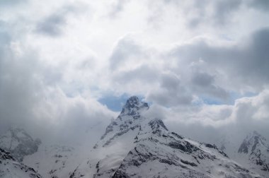 Kış akşamında buzla kaplı gri yüksek dağ zirveleri ve bulutlarla kaplı gökyüzü. Kafkas Dağları, Dombay bölgesi, Belalakaya Dağı.