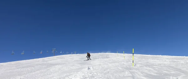 Panoramic view on snowy ski slope with skier and sk-lift at sunny winter day. Caucasus Mountains, Georgia, region Gudauri. Wide-angle view
