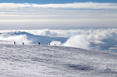 Kar yamacında kayakçıların ve snowboardcuların siluetleri ve kış akşamları güzel bulutlarda dağların üzerinde. Kafkasya Dağları, Gürcistan, Gudauri bölgesi.