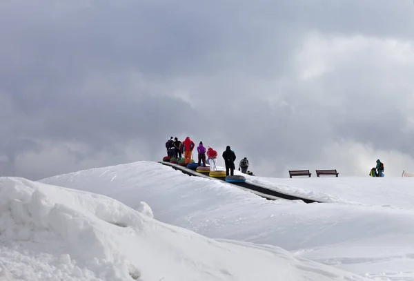 Stock image People move up on moving carpets with snow tube at ski resort and snowy slope with gray cloudy sky. Caucasus Mountains, Georgia, region Gudauri at winter.