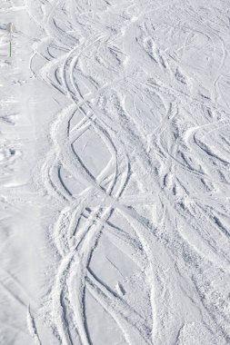 Güneşli kış gününde kayak ve snowboard izleri olan karlı bir kayak yamacı.