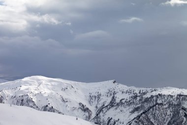 Güneş ışığı karlı dağlar ve kış akşamları bulutlu gri gökyüzü. Kafkas Dağları, Gürcistan 'ın Svaneti bölgesi.